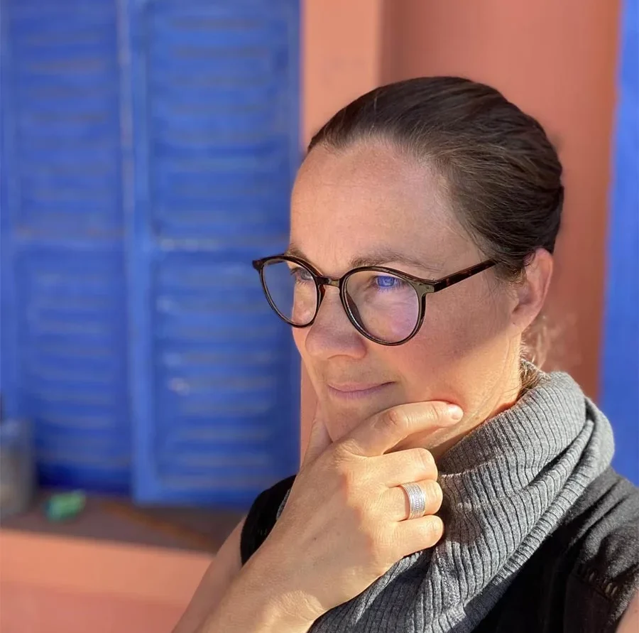 Artikelbild ueber mich Vanessa Lagnach Frau mit Brille und kurzem Haar, nachdenklicher Ausdruck vor bunter Häuserwand.